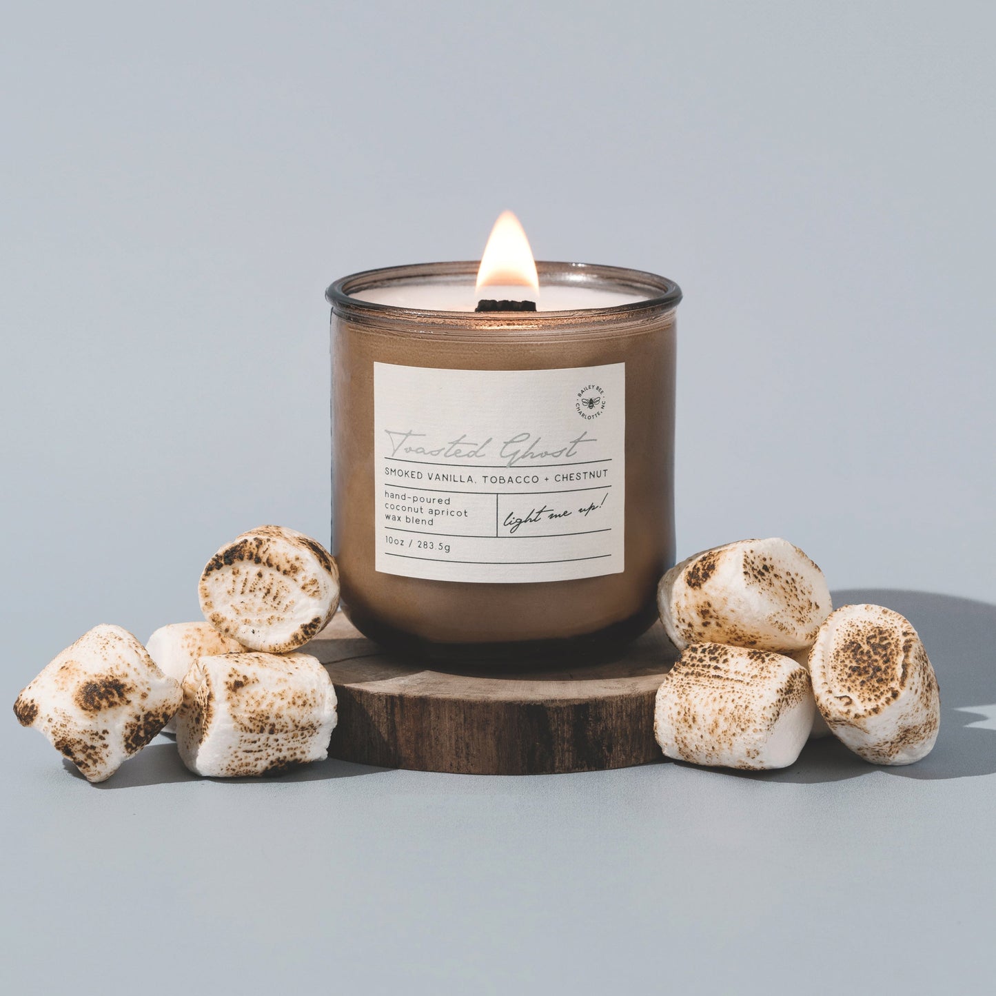 Candle with a label on a wooden stand surrounded by decorative items against a light gray background