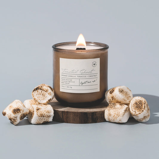 Candle with a label on a wooden stand surrounded by decorative items against a light gray background