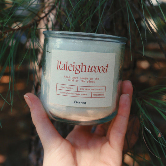 hand holding raleighwood classic candle against pine backdrop