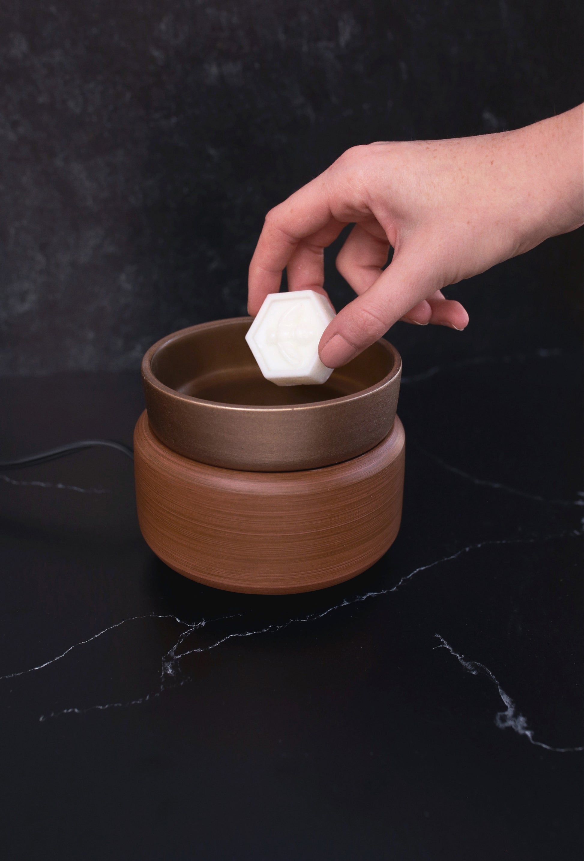 hand placing wax melt into bronze and walnut wax warmer